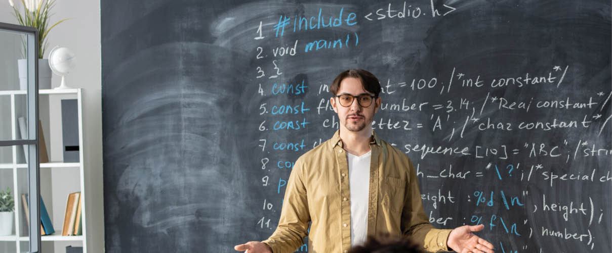 Confident teacher of modern technology course standing against blackboard in front of audience and explaining lesson points
