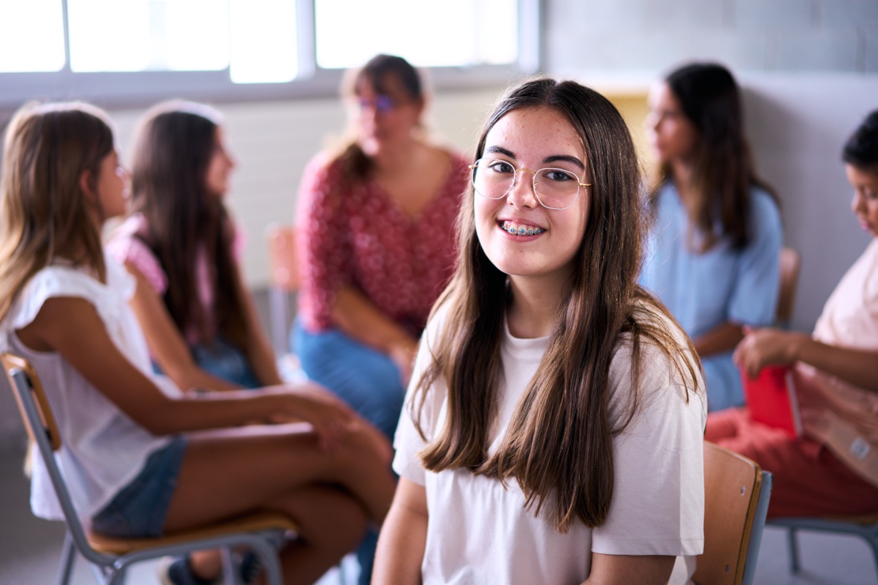 Portrait nerd Caucasian primary girl student sitting in class with classmates in background.